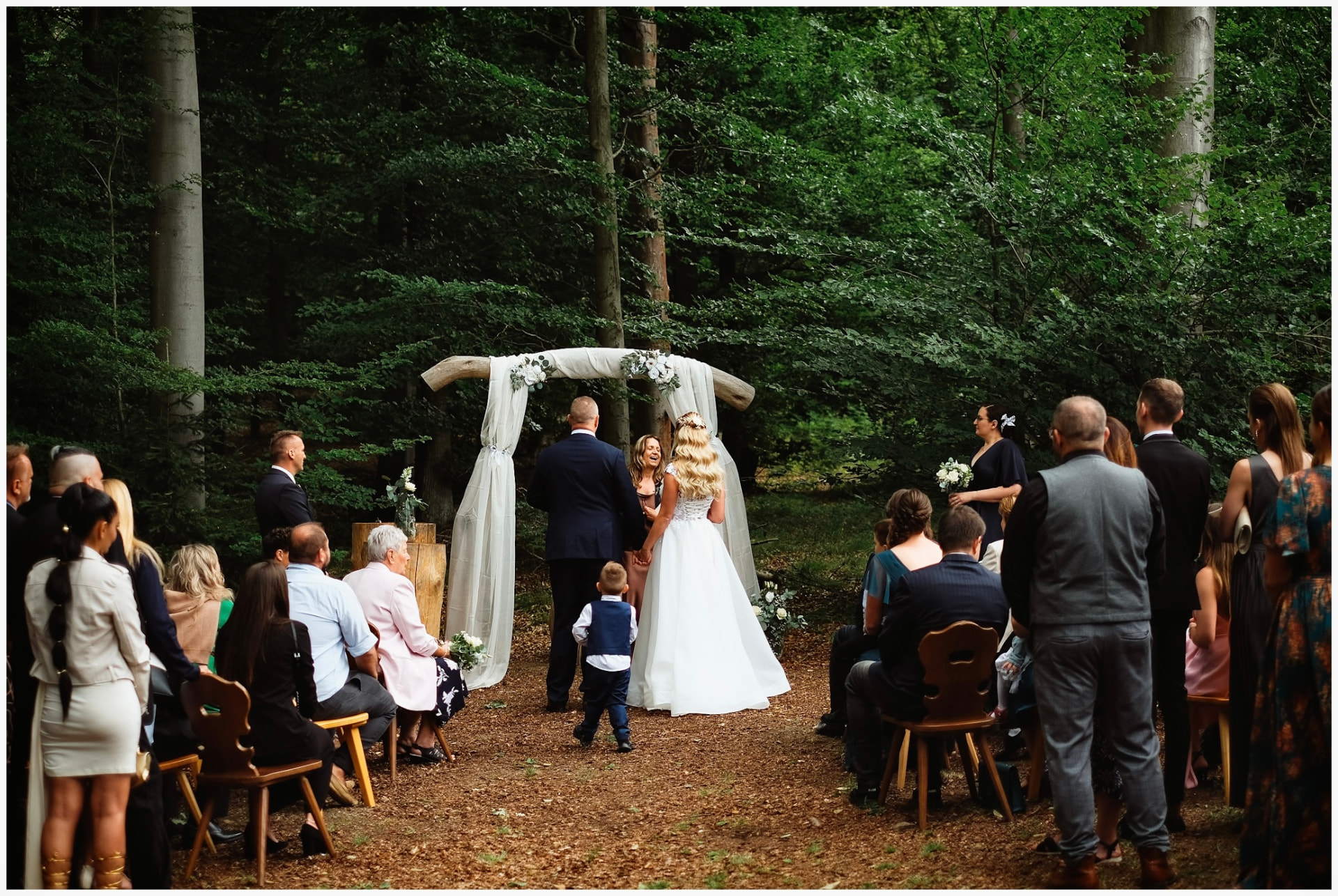 Outdoor wedding ceremony beneath a wooden arch in the forest