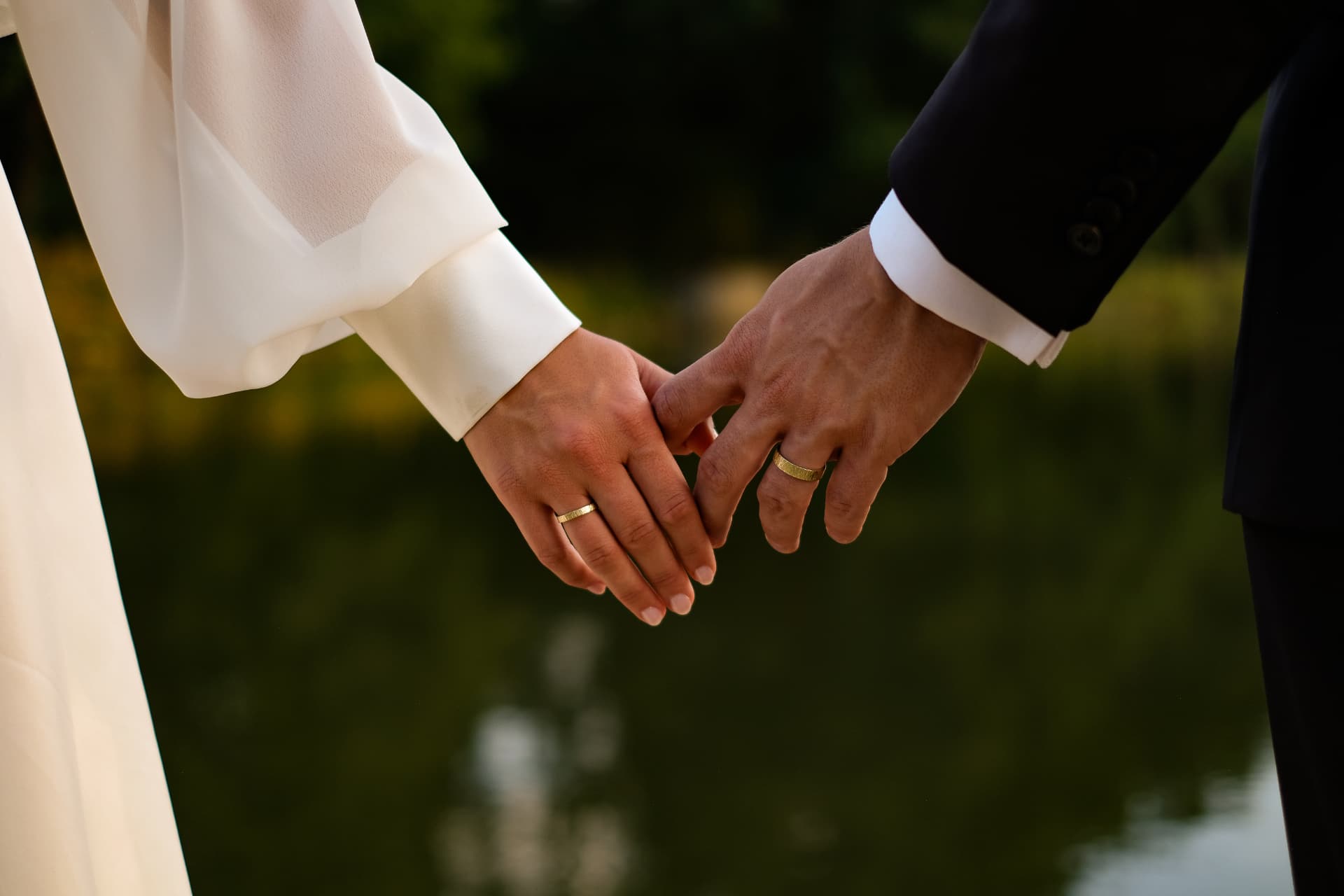 Bride and groom holding hands with wedding rings by the water