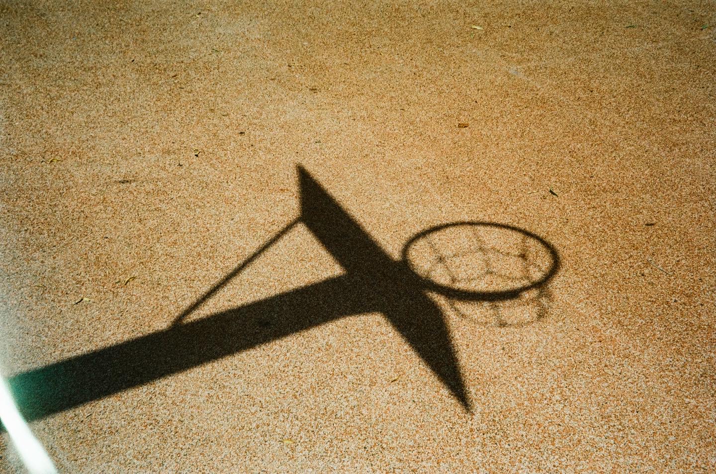 Shadow of a basketball hoop on a sunlit court