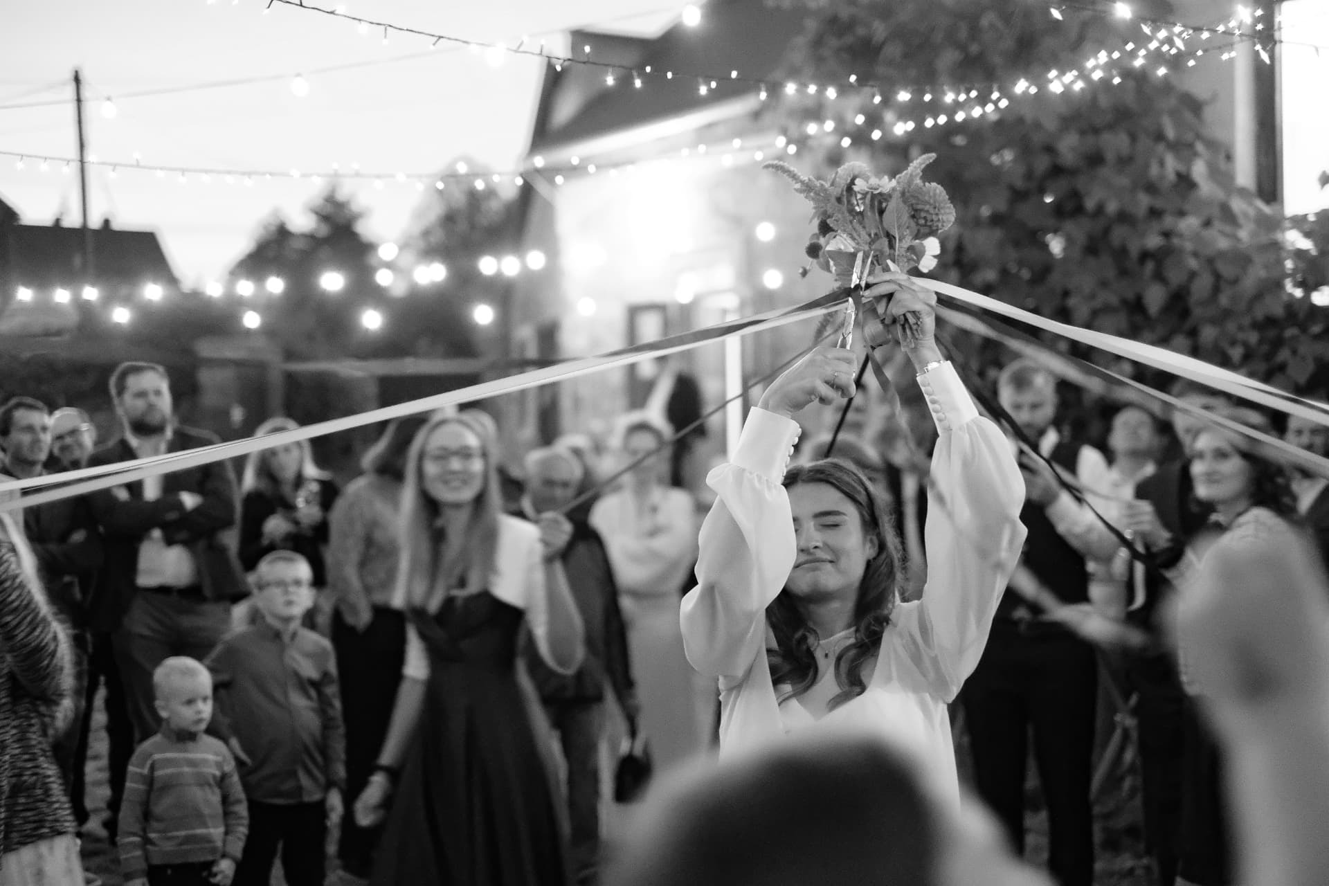 Bride raising her bouquet beneath string lights