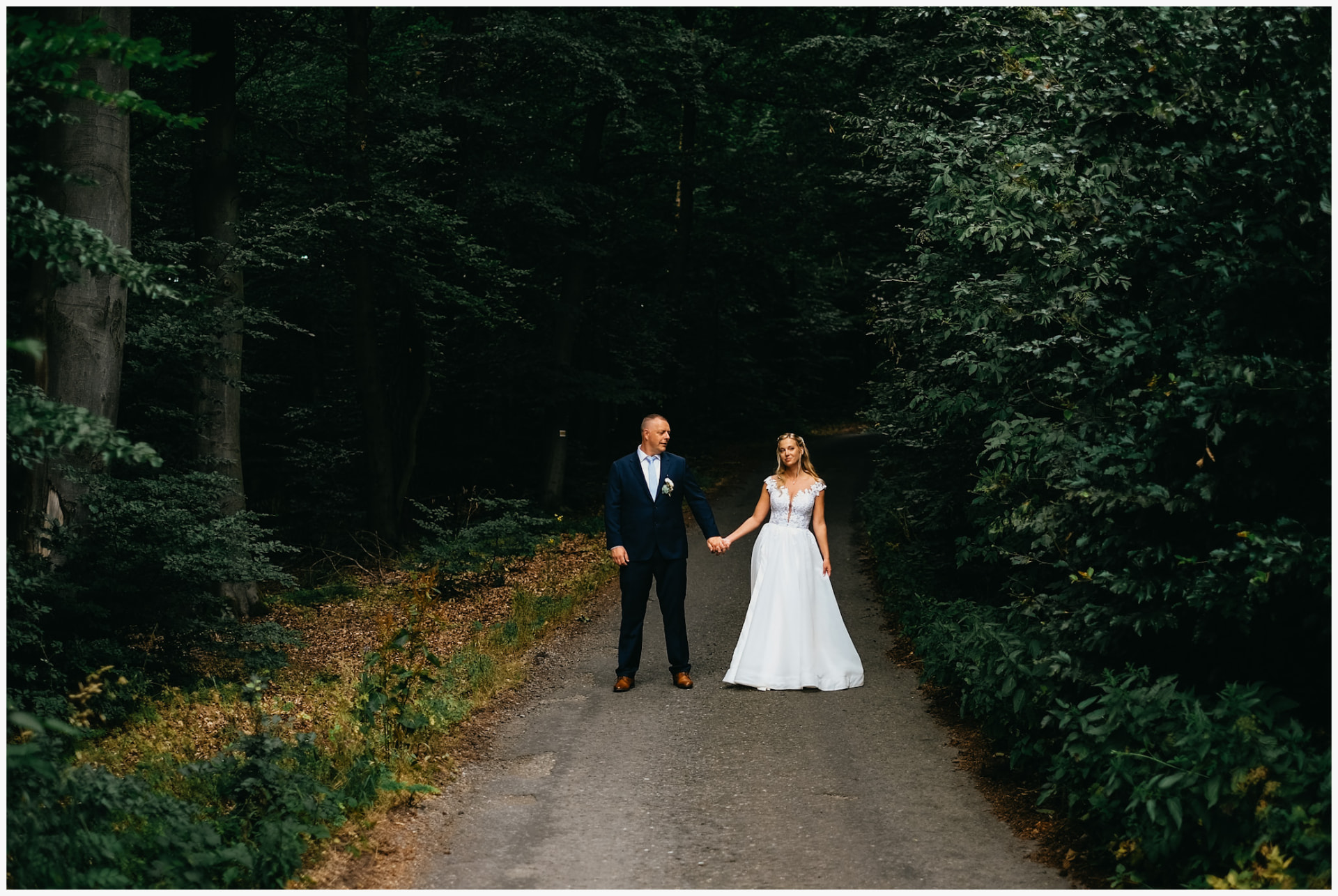 Newlyweds holding hands on a dark forest road