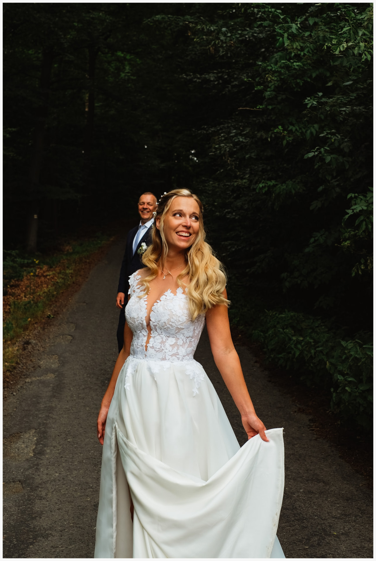 Bride laughing on a forest path with the groom behind her